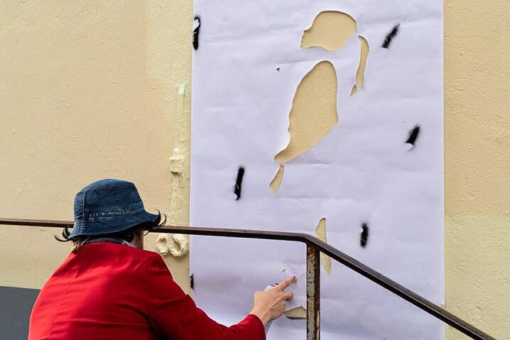 Eine Person befestigt eine Papierschablone an einer Außenwand in der Flensburger Innenstadt. Die Schablone zeigt ein Mädchen, dass in die Luft schaut.