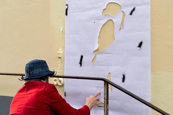 Eine Person befestigt eine Papierschablone an einer Außenwand in der Flensburger Innenstadt. Die Schablone zeigt ein Mädchen, dass in die Luft schaut.