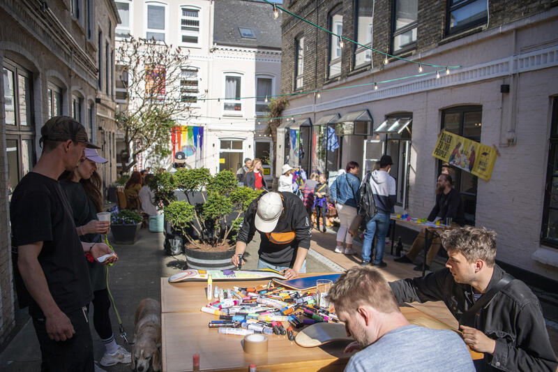 Menschen sitzen an Tischen im Käte-Lassen-Hof Flensburg und bemalen Skateboards. Andere schlendern durch den Hof und tauschen sich aus.