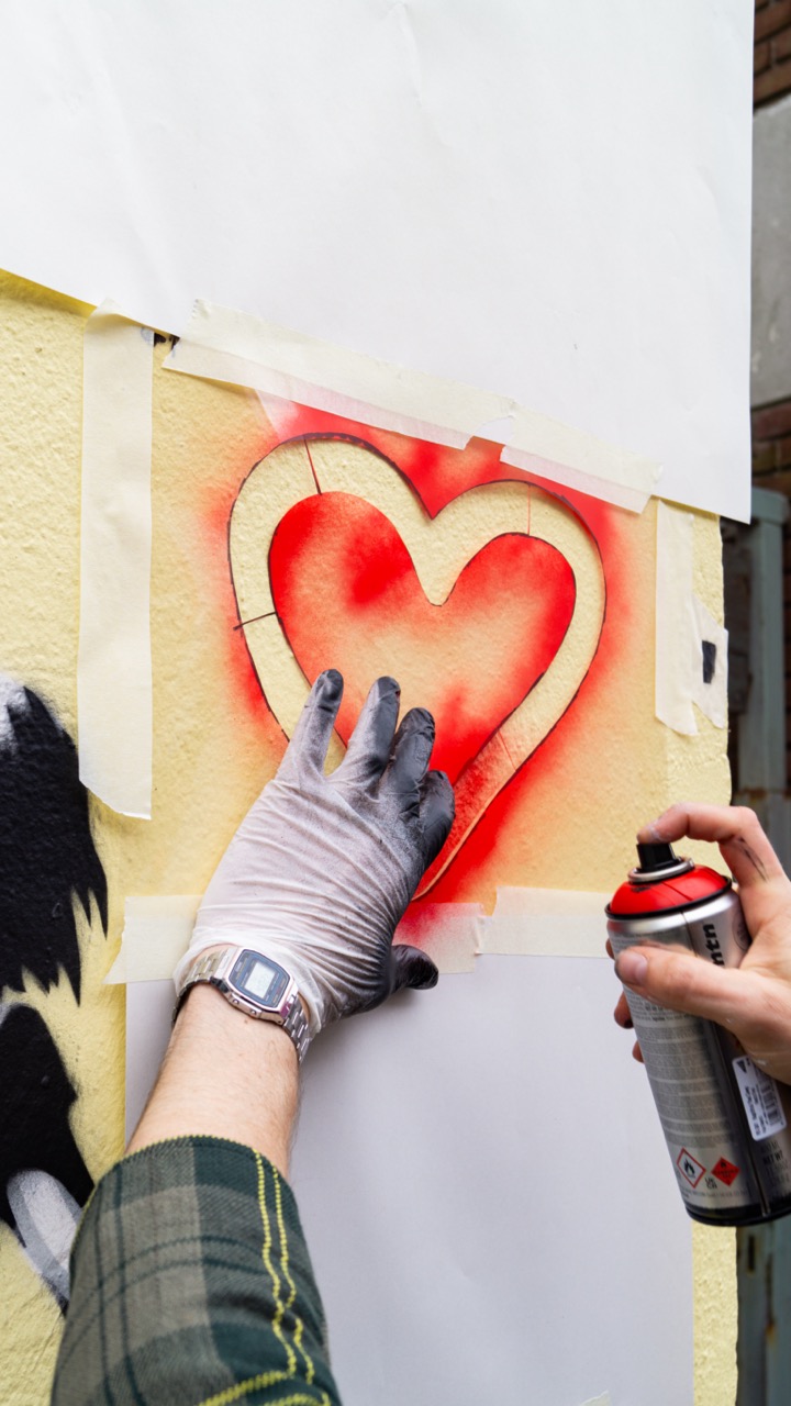 Eine Person sprayt den Umriss eines roten Herzens an eine Außenwand.