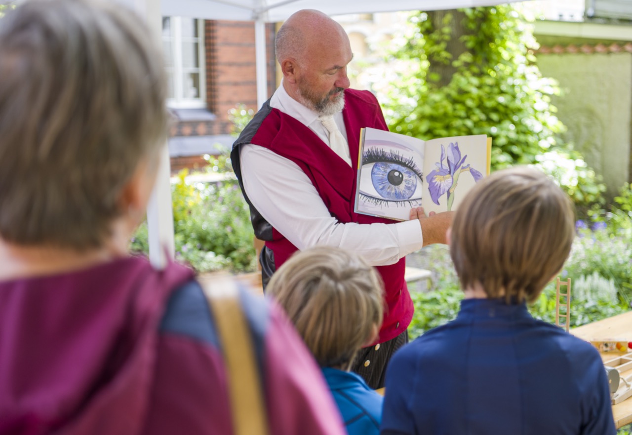 Ein stehender Mann zeigt Kindern die Innenseiten eines Buches.